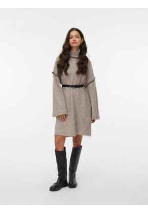 Strickkleid in Hellbraun mit Rollkragen, langen Ärmeln und Fransen-Saum. Kombiniert mit einem schwarzen Gürtel und kniehöhen schwarzen Stiefeln.