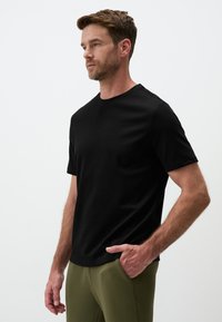 Czarna koszulka z krótkim rękawem w klasycznym kroju, wykonana z miękkiej tkaniny. Posiada okrągły dekolt i wygodne dopasowanie, zestawiona z oliwkowymi spodniami.