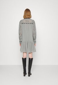 Vestido gris con falda en capas, mangas largas con volumen y una pechera con diseño de encaje. Combinado con botas de cuero negras hasta la rodilla.