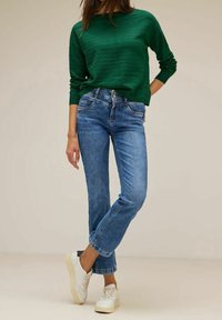 Grüner gerippter Pullover mit langen Ärmeln, kombiniert mit hellblauen Straight-Leg-Jeans und weißen Sneakers. Einfache, lässige Outfit-Gestaltung.