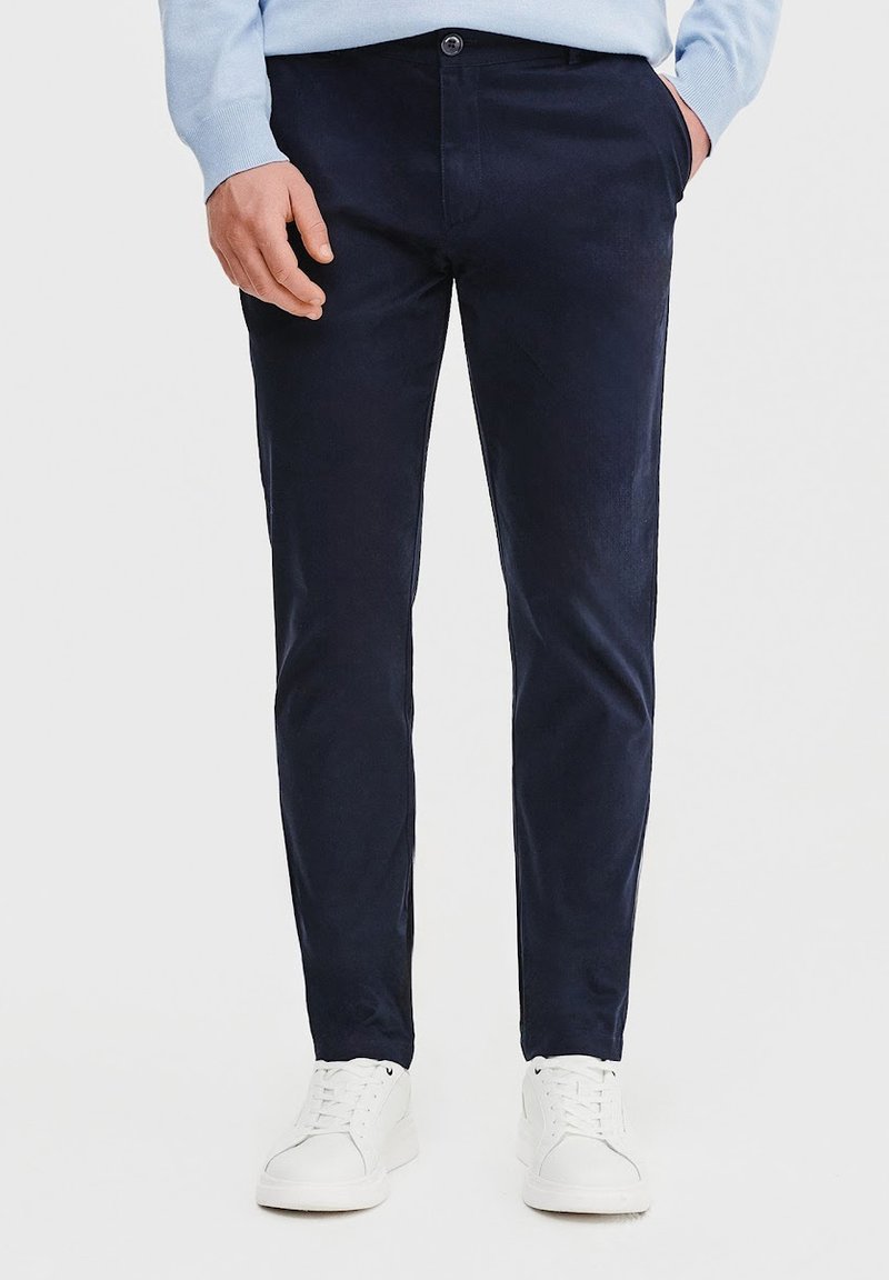 Granatowe spodnie z korduroju o dopasowanym kroju, z przednimi kieszeniami i zapięciem na guzik. Połączone z białymi trampkami dla uzyskania pełnego wyglądu.