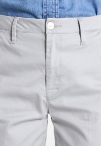 Pantaloni grigi chiari con vestibilità slim, dotati di vita standard, chiusura con bottone e dettagli di cucitura discreti lungo le tasche.