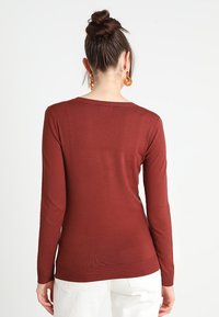 Langarm, rostfarbener Pullover aus weichem, feinem Strickmaterial. Hat einen runden Ausschnitt und einen gerippten Saum für einen figurnahen Stil.