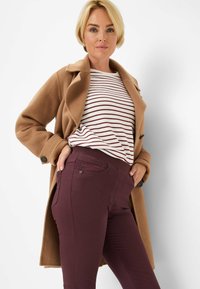 Kameelcoat met een notch-kraag, gestreept wit en kastanjebruin shirt, en kastanjebruine slim-fit broeken met zijzakken en een gestructureerde afwerking.