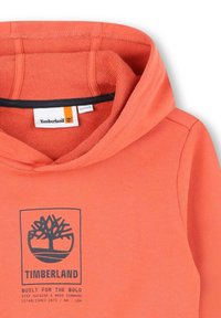 Sweatshirt à capuche orange corail avec un logo graphique bleu foncé comprenant un arbre et du texte. Présente un tissu doux et texturé avec des finitions contrastées.