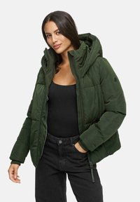 Grüne Pufferjacke mit Kapuze, mit einer gesteppten Textur, Front-Reißverschluss und zwei Seitentaschen, getragen über einem schwarzen Oberteil und dunklen Hosen.