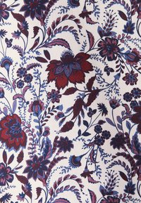 Motif floral complexe avec des fleurs rouges et bleues, des feuilles et des vignes sur un fond en tissu blanc texturé.