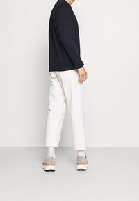 Felpa blu navy con colletto rotondo e orlo a costine, abbinata a pantaloni color crema. Vengono indossate sneaker color cuoio con suole bianche.