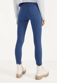 Blue and black checkered leggings made of stretchy material, featuring a high waist and back pockets, paired with chunky white boots.