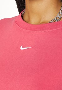 Rosa bomulls-tshirt med rundad halsringning, med en liten vit Nike-logga på bröstet. Mjuk textur, avslappnad design, medel tjocklek.