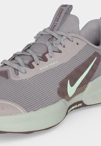 Gros plan d’une chaussure de course Nike Trail grise avec une tige en maille texturée, des lacets réfléchissants, un logo Swoosh blanc et une semelle amortie.