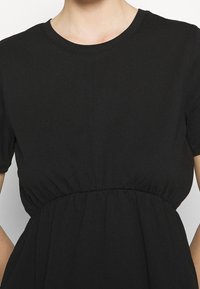 Vestido negro de manga corta con detalle de cintura fruncida, llevado por una persona, mostrado de cuello a cintura sobre un fondo liso.