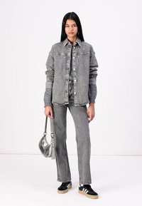 Veste en denim grise avec des clous, assortie à un pantalon en denim gris. Portée avec des baskets noir et blanc et un sac à main argenté.