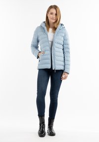 Chaqueta de plumas de color azul claro con capucha, costuras horizontales, cremallera frontal y dos bolsillos laterales, combinada con jeans oscuros y botas negras hasta el tobillo.