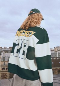 Grön och vit randig sweatshirt med "MICKEY" i gult och "28" i blått på baksidan. Svalkande tyg, avslappnad passform och långärmad.