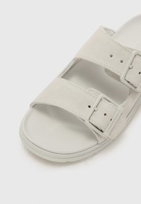 Grå semsket sandal med to justerbare stropper og spenneakenter. Gummisåle med teksturert mønster for grep. Minimalistisk design.