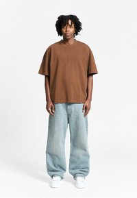 Brun kortærmet t-shirt med rund hals, sammen med lyseblå løstsiddende jeans og hvide sneakers. Enkelt design uden mønstre.