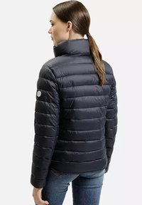 Granatowa kurtka puchowa z wysokim kołnierzem, poziomym wzorem na baffles oraz akcentem logo, zestawiona z dżinsami. Gładka, błyszcząca tekstura.