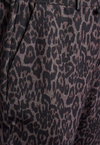 Tissu à motif léopard avec des taches marron foncé sur un fond marron clair, présentant une texture lisse et des détails de plis soignés.