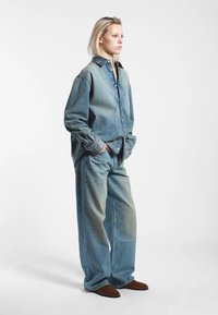 Ljusblå denimskjorta i översized modell och matchande vida jeans med knappstängning, framfickor och naturlig blekning. Bruna slip-in skor.