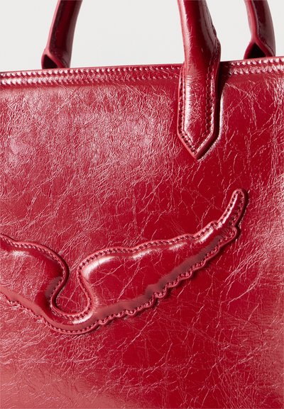 Κόκκινη δερμάτινη τσάντα χειρός με γυαλιστερό φινίρισμα και ραμμένη λεπτομέρεια σε σχήμα φτερού κοντά στη λαβή στην κορυφή.