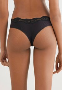 Zwarte bikinionderbroek met kantafwerking, gemaakt van gestructureerde stof, met een lage taille en golvende randen langs de tailleband.