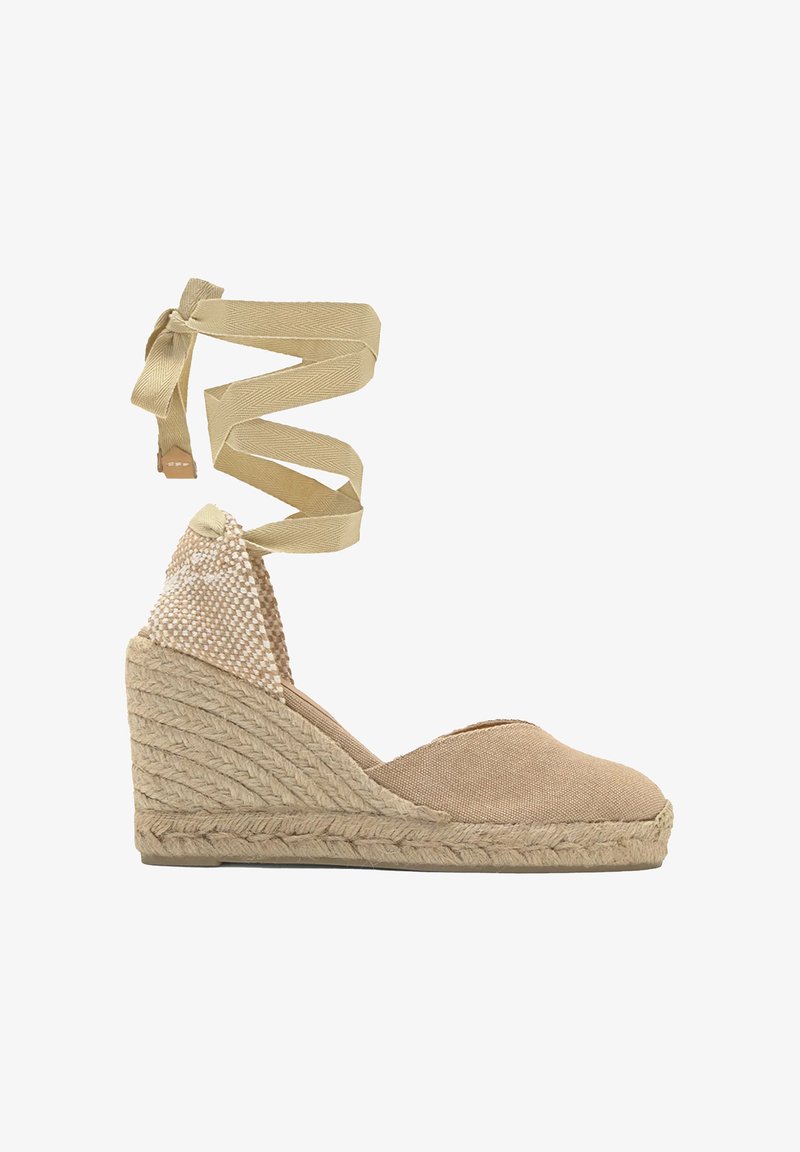 Espadrille compensée en toile beige avec semelle en jute tressé et bride à nouer autour de la cheville, présentant un détail tissé sur le talon.