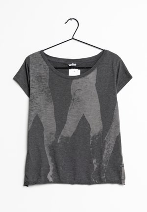 Ciemnoszara koszulka z krótkim rękawem na wieszaku z wyblakłym abstrakcyjnym nadrukiem przypominającym idące nogi w jaśniejszych odcieniach szarości.