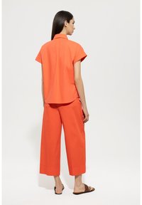 Orange cotton shirt with short sleeves and a subtle back pleat, paired with matching wide-leg pants. Features a relaxed fit and stitched hems.