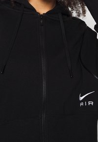 Svart zip-up huvtröja tillverkad av bomullsblandat tyg. Har en framfickauppdragning, snoddar och vit "Nike AIR" logotyp på vänster bröstområde.
