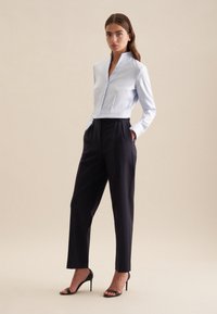 Camicia azzurro chiaro con colletto e chiusura a bottoni abbinata a pantaloni navy a vita alta e tacchi a spillo neri su uno sfondo neutro.