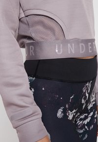 Violetti pitkähihaine paita, jossa on verkko-yksityiskohtia ja harmaa nauha. Mustissa legginsseissä on kukkakuosi violetin ja valkoisen sävyissä.