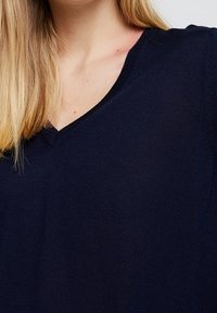 Pull en maille douce bleu marine à col en V ; doté d'un col côtelé et d'une coupe décontractée, avec une texture lisse visible.