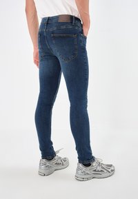 Tajta jeans i mörkblå denim med bakfickor och ett märkesband. Kombineras med grå löparskor med silverdetaljer.