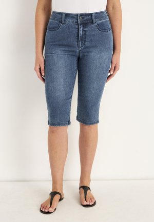 Denim bermuda shorts in donkerblauw met een aansluitende taille, vijf zakken en omgeslagen zoom. Gecombineerd met zwarte slippers op blote voeten.