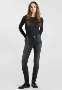 Jean skinny noir taille haute en denim extensible, avec poches avant, fermeture à bouton et une finition légèrement délavée.