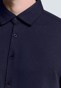Navy blauwe button-up shirt met een visgraatstructuur, een klassieke kraag en zwarte knopen, met een gestructureerd ontwerp en soepel materiaal.