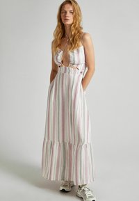 Dryžuota maksi suknelė balta, rožine ir pilka, su volaniniu apdailu, iškirptomis šoninėmis dalimis ir reguliuojamomis spaghetti petnešėlėmis. Dėvima su sportiniais bateliais.