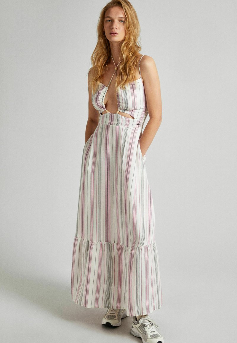 Dryžuota maksi suknelė balta, rožine ir pilka, su volaniniu apdailu, iškirptomis šoninėmis dalimis ir reguliuojamomis spaghetti petnešėlėmis. Dėvima su sportiniais bateliais.