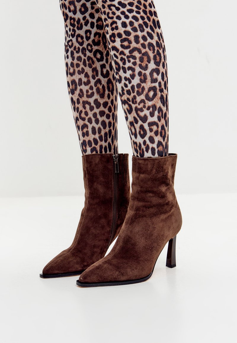 Bruine suède enkellaarsjes met een spitse neus, rits aan de zijkant en een slanke stilettohak. Draagt met een legging in luipaardprint.