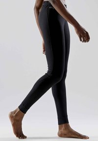 Black athletic leggings with a ribbed texture, fitted design, elastic waistband, and ankle cuffs, shown on a model's leg in motion.