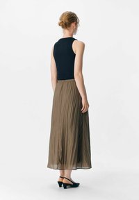 Top sin mangas negro, falda maxi plisada marrón y zapatos de tacón negros. Enfócate en la textura de la tela y el diseño fluido de la falda.