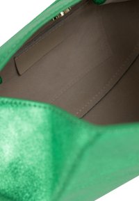 Intérieur de sac à main métallique vert, texture lisse, poche zippée, doublure beige, forme triangulaire. Les bords cousus apportent de la structure.