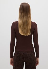 Braunes, geripptes Langarmoberteil mit figurbetonter Form, kombiniert mit dunkelbraunen, leo-print Hosen mit glatter Textur und feinen Nahtdetails.