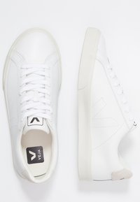 Baskets blanches avec design à lacets, matériau en cuir lisse, semelle en caoutchouc et branding discret. Accent beige doux au talon.