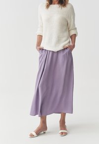 Suéter de punto ligero en color crema combinado con una falda midi fluida en lavanda. La falda cuenta con bolsillos laterales; los zapatos son sandalias blancas de slide.
