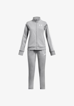 Svetlo siva trenirka z jopico z zadrgo in usklajenimi hlačami z belimi logotipi Under Armour na prsih in stegnih.