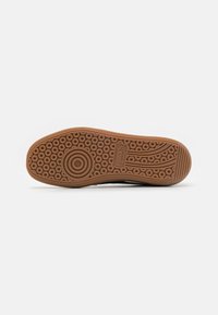 Semelle de chaussure avec motif de bande de roulement circulaire en caoutchouc marron, avec logo Puma et texte "moda" embossé au centre.