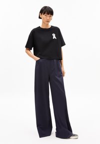 Black cropped t-shirt with a white emblem, paired with loose, navy blue wide-leg pants, featuring a smooth fabric and relaxed fit.