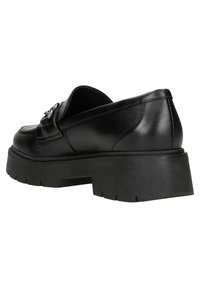 Chaussures à enfiler en cuir noir avec une semelle plateforme épaisse, ornées de ferrures décoratives et d'une texture lisse. Vue arrière mettant en valeur des lignes épurées.